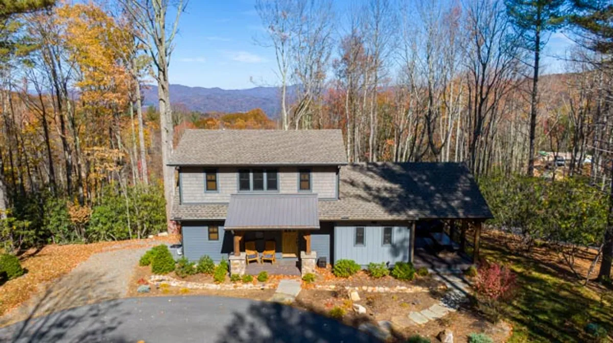 A serene exterior view of the house with a welcoming porch, surrounded by tall trees and dramatic mountain scenery. The setting is ideal for family gatherings, nature walks, and relaxing while taking in the breathtaking Blue Ridge Mountain views.