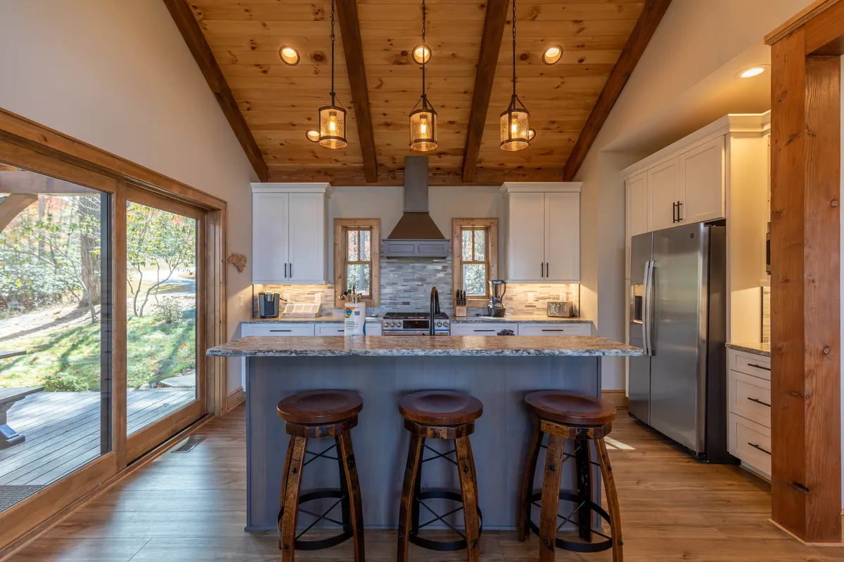 This image features the kitchen island with stools, pendant lighting, and a window view, spotlighting the area for cooking and gathering. The layout is open, with space for both meal preparation and social interaction, ideal for breakfasts before a hike or festive dinners.