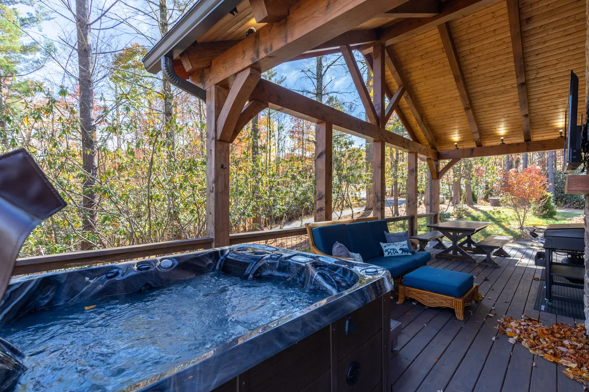 A tranquil deck area features a hot tub with panoramic mountain views, a cozy seating area, and a well-equipped outdoor kitchen. The wood beams and natural setting invite relaxation and gathering, whether for morning coffee or evening stargazing.