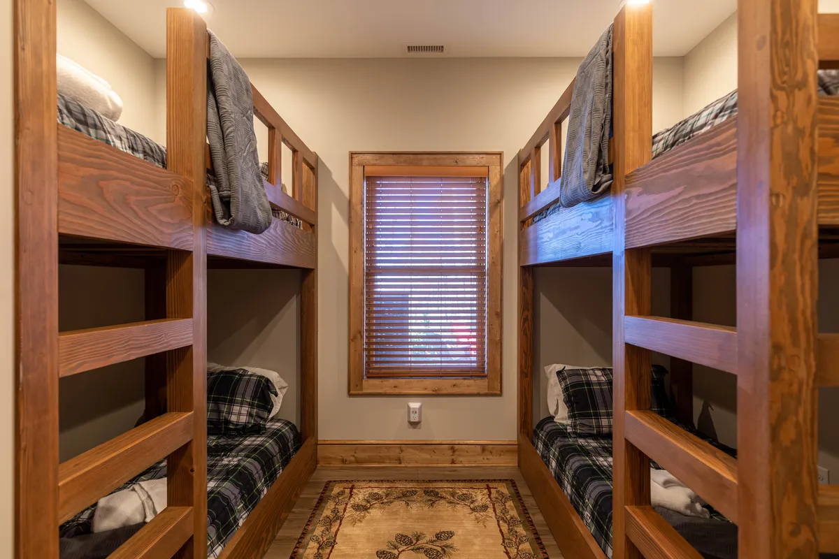 A custom bunk room with sturdy wooden bunk beds, a window offering natural light, and a soft rug on the floor. The layout is playful and inviting, perfect for children or teens seeking an adventurous sleepover experience.