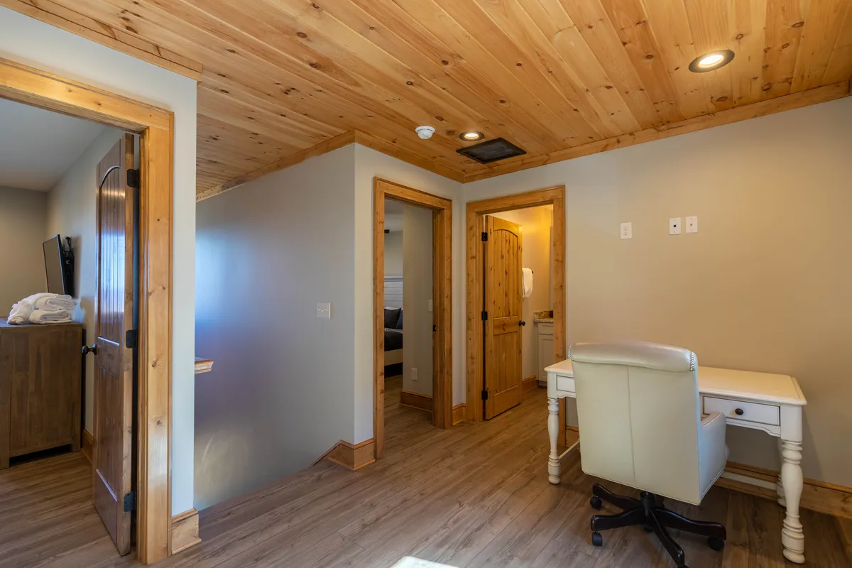 A cozy, functional workspace with a wooden ceiling, a dedicated desk and chair, and doorways leading to other parts of the home. The area is bathed in warm light, providing an ideal setting for focused work or study.